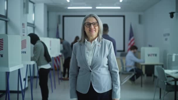 ビジネスウーマンは現代の投票所 ポーズ カメラ 笑顔に立っています 成熟した女性の肖像画 アメリカ合衆国選挙の有権者 投票ブースとアメリカの国旗の背景 — ストック動画