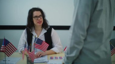 Kadın anket memuru oy kullanma merkezindeki kayıt masasında oturuyor, Afrikalı Amerikalı erkek seçmenlerle konuşuyor ve gazete bülteni veriyor. Birleşik Devletler 'de seçim günü. Vatandaşlık görevi ve demokrasi.