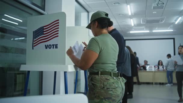 女性兵士とアジア女性が投票所のブースで投票 アメリカ合衆国選挙の日 アメリカ合衆国大統領候補の政治的競争 愛国心と市民の義務 ドリー ショット — ストック動画