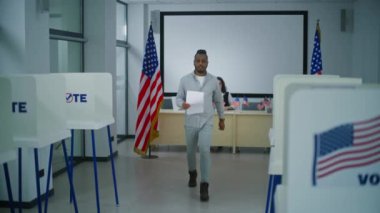Afro-Amerikalı adam oy kullanma merkezindeki oy kullanma memurundan oy almak için kağıt oy kullanıyor. Amerikan vatandaşı bülteni doldurmak için oy kabinine yürüyor. Amerika Birleşik Devletleri 'nde seçim günü. Yurttaşlık görevi.