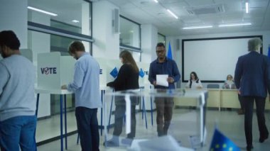 AB seçimleri sırasında sandık merkezindeki oy kullanma kabinlerinde çok ırklı seçmenler veya Avrupalı insanlar oy kullanıyor. Afro-Amerikalı kadın ve erkek ilan kutusuna koydular. Avrupa Birliği 'nde Seçim Günü. Yurttaşlık görevi.