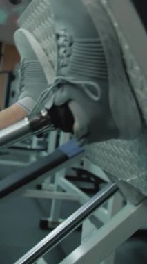 Modern spor salonunda ya da fitness merkezinde protez bacaklı bir sporcunun bacak pres makinesinde egzersiz yaparken dikey görüntüsü. Fiziksel engelli formda bir adam profesyonel spor kullanarak güçlü bir antrenman yapıyor.