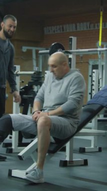 Modern spor salonunda halterli protez bacak egzersizleri ve kişisel fitness koçu olan dikey nişancı. Yapay bacaklı bir atlet spor ekipmanları kullanarak ağırlık çalışması yapıyor. Fiziksel