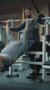 Modern spor salonunda halterli protez bacak egzersizleri ve kişisel fitness koçu olan dikey nişancı. Yapay bacaklı bir atlet spor ekipmanları kullanarak ağırlık çalışması yapıyor. Fiziksel