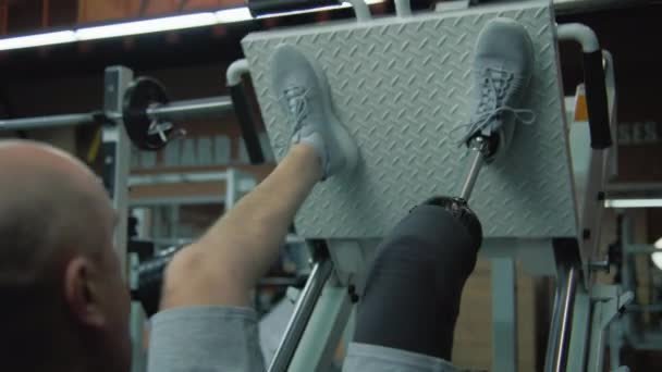 モダンなジムで脚プレス機の義足列車で動機づけられたスポーツマン 身体障害のあるアクティブスポーツマンは スポーツ機器を使用して強度トレーニングを行います ボディポジティブコンセプト — ストック動画