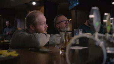 İki erkek arkadaş konuşuyor, bar tezgahında oturup hafta sonunu kalabalık bir barda geçiriyorlar. Televizyonda yayınlanan futbol maçının arka planında. Yaşam tarzı ve eğlence anlayışı.