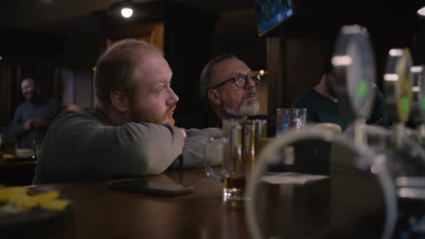 两个男性朋友聊天 坐在酒吧柜台边 在拥挤的酒吧度过周末的夜晚 电视屏幕上播放了足球比赛的现场直播 生活方式和休闲的概念 — 图库视频影像