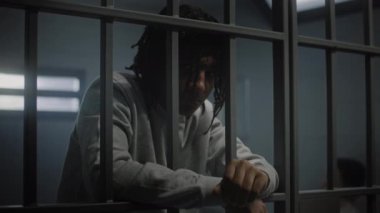 Ciddi Afro-Amerikalı dövmeli genç hapisteki hücrede duruyor ve kameraya bakıyor. Genç suçlu, suçtan hapis cezasına çarptırıldı. Gençlik Gözaltı Merkezi ya da Cezaevi.