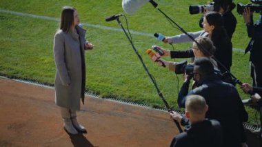 Futbol takımı direktörü basın sorularını cevaplıyor ve maçtan önce futbol sahasının yakınında röportaj veriyor. Haber muhabirlerinin doldurduğu özel yatırımcı kadın. Basın konferansında ilham verici bir konuşma..