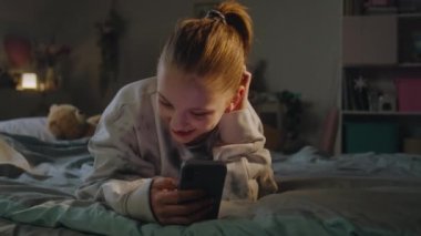 Çekici bir genç kızın cep telefonuyla görüntülü konuşma yaptığı yakın plan. Beyaz tenli gençler akşamları rahat yataklarda yatarlar. Gençler hafta sonunu evdeki rahat yatak odasında geçirirler..
