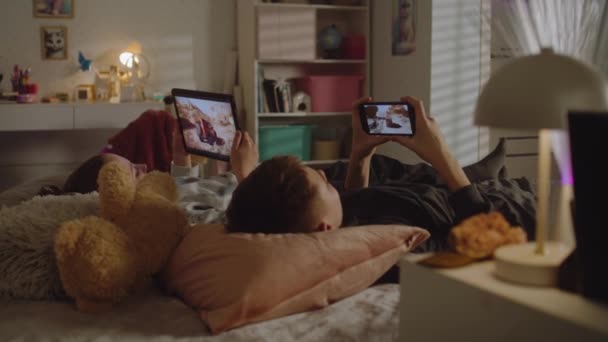 Двоє Підлітків Лежать Ліжку Своїй Кімнаті Грають Відеоігри Цифрових Пристроях — стокове відео