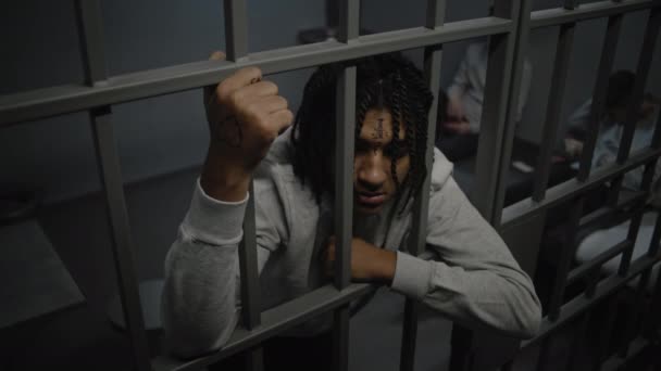 愤怒的非洲裔美国少年囚犯站在监狱的牢房里 手里拿着铁棍 年轻囚犯在床的后面打牌 青少年拘留中心或教养所 高角度 — 图库视频影像