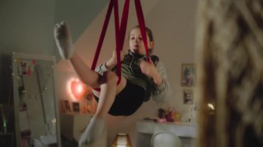 Genç kız büyük ışıklı yatak odasında hava jimnastiği yapıyor. Kafkasyalı genç, konfor odasının ortasında akrobatik egzersizler yapmak için hava jimnastik kurdeleleri kullanıyor. Gençler hafta sonunu ve trenleri evde geçirir..