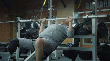 Modern fitness merkezinde boş halterli protez bacaklı motive bir sporcu, sonra ara veriyor. Fiziksel engelli sporcu, spor aletlerini kullanarak egzersiz yapar.