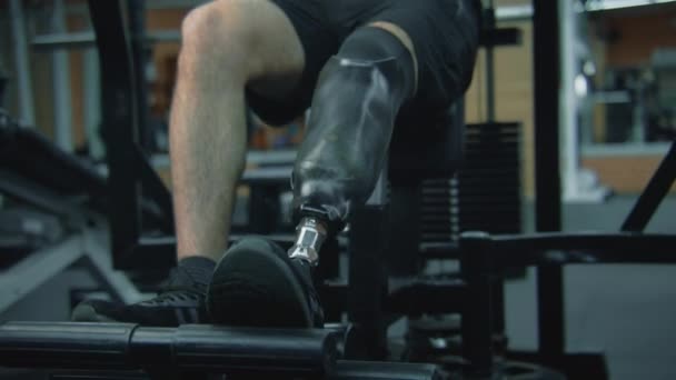モダンなフィットネスルームやジムでトレーニングマシン上の足のトレーニングで義足で動機づけられた運動選手 身体障害のある大人のスポーティな男性は プロスポーツ機器を使用して強度トレーニングを行います — ストック動画