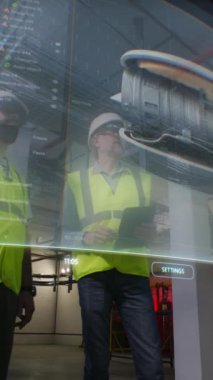İstasyonda sanal rüzgar türbini ve 3 boyutlu hologram kullanan elektrik hatlarının detaylarını izleyen iki erkek çalışan. Modern ve dijital elektrik üretim sistemi. Dikey çekim
