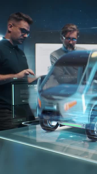 2人の男性自動車エンジニアがタブレットコンピュータと拡張現実ホログラムを使用して電気エンジンを搭載した新しい環境に優しいトラックを開発 自動車ハイテク開発の3Dグラフィック バーティカルショット — ストック動画