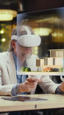 Erkek tasarımcı VR kulaklık ve kablosuz kontrolör kullanır, mimari proje yapar, sanal gerçeklikte ev dış tasarımı yaratır. Modern yüksek teknoloji şirketi. Üç boyutlu hologram. Dikey çekim