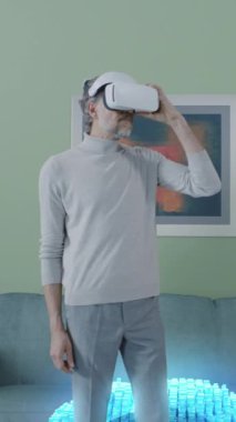 Yetişkin bir erkeğin sanal gerçeklik gözlüğü takıp evdeki internet sayfalarına göz attığı görüntüyü büyüt. Dikey çekim