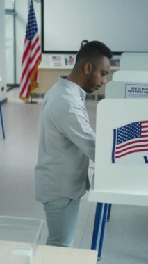 Afro-Amerikalı bir adam oy kullanma merkezindeki oy kullanma kabininde başkan adayı için oy veriyor, sonra da kağıt sandığa koyuyor. ABD 'de Ulusal Seçim Günü' nde erkek ABD vatandaşı. Yurttaşlık görevi.