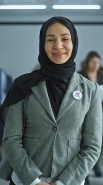 Kadın modern bir seçim merkezinde duruyor, poz veriyor, gülümsüyor ve kameraya bakıyor. Arap kadın portresi, Amerika Birleşik Devletleri seçmeni. Oy verme kabinleri olan bir arka plan. Yurttaşlık görevi kavramı.