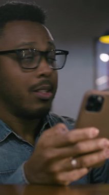 Afrikalı Amerikalı adamın dikey çekimi, futbol takımının şampiyonluk zaferine seviniyor, bahisçi reytinglerini telefonla kontrol ediyor. Happy fanatiği barda oturarak futbol maçı bahsini kazanıyor.