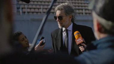 TV haberleri için basın toplantısında başarılı bir özel yatırımcı. Organizasyon temsilcisi basın sorularını yanıtlıyor ve bir futbol stadyumunun dışında röportaj veriyor. Gazeteciler basın kampanyasında kalabalıklar.