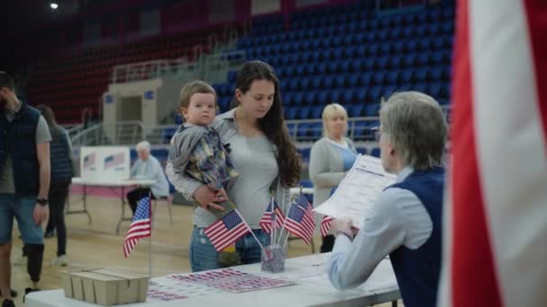 美国女性公民在投票站投票 手里拿着婴儿的妇女与投票官员交谈并发布公告 美国总统候选人的政治竞争 全国选举日 — 图库视频影像