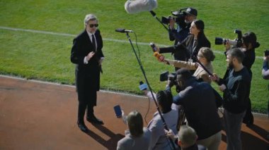 SEO ya da futbol takımı yöneticisi, önemli maçtan önce basın sorularını yanıtlıyor ve futbol sahasının yakınında röportaj veriyor. Özel yatırımcı ya da iş adamı gazetecilerle dolup taşıyor. Basın toplantısı.