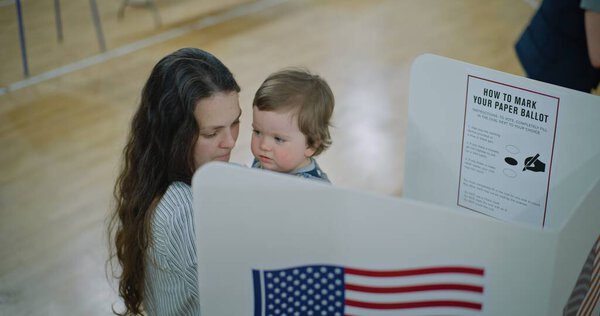 Американские граждане приходят голосовать на избирательном участке. Избирательница с ребенком на руках стоит у кабины для голосования. Политические гонки кандидатов в президенты США. Национальный день выборов. Гражданский долг. Долли выстрелил.