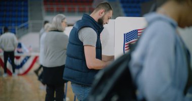 Elinde bülten olan kadın seçmen oy verme kabinine geliyor. Amerikan vatandaşları oy kullanma merkezine oy vermeye geldi. ABD başkan adaylarının siyasi ırkları. ABD 'de Ulusal Seçim Günü.