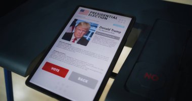 ZAPORIZHYA, UKRAINE - 15 Mart 2024: Tablet bilgisayarlı oy kullanma kabini. Donald Trump ve tablet ekranda gösterilen düğmeler hakkında bilgi. Oylama için modern dijital teknoloji. Başkanlık