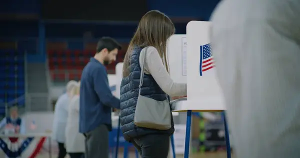 白人女性の有権者は投票ブースへの掲示書が付属しています アメリカ国民は投票所で投票する アメリカ合衆国大統領候補の政治的競争 アメリカ合衆国選挙の日 — ストック写真