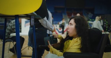 Kadın seçmen, SMA tekerlekli sandalyedeki kadın oy kullanma kabininde oy veriyor. Özürlü ABD vatandaşı oy vermek için uzaktan kumanda düğmeleri kullanıyor. Amerika Birleşik Devletleri Başkanlık Seçimleri.