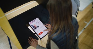 Beyaz kadın tablet bilgisayar kullanarak ABD başkan adayı seçimleri yapıyor ve oy veriyor. ABD 'de Ulusal Seçim Günü' nde oy kullanma merkezindeki ABD vatandaşı. Yüksek açı.