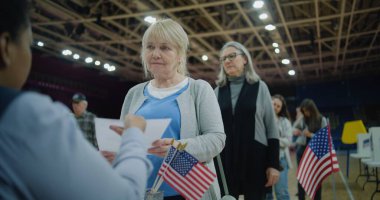 Yaşlı kadın anket memuruyla konuşuyor ve bülten alıyor. Amerikan vatandaşları oy kullanma merkezine oy vermeye geldi. Birleşik Devletler 'de Ulusal Seçim Günü. ABD başkan adaylarının siyasi yarışları.
