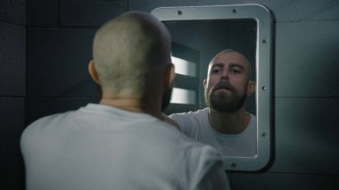 Erkek suçlu yüzünü havluyla siler ve hapishane hücresindeki aynada kendine ciddi ciddi bakar. Mahkum, hapiste işlediği suçtan hapis cezasına çarptırıldı. Gözaltı merkezi ya da ıslah evi.