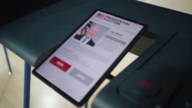 ZAPORIZHYA, UKRAINE - 15 Mart 2024: Tablet bilgisayarlı oy kullanma kabini. Joe Biden ve tablet ekranında gösterilen düğmeler hakkında bilgi. Oylama için modern dijital teknoloji. Başkanlık