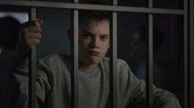 Yüzünde dövme olan beyaz bir genç hapisteki hücrede duruyor, metal parmaklıklar tutuyor ve kameraya bakıyor. Arka planda çeşitli genç mahkumlar konuşuyor. Çocuk ıslahevi ya da ıslah evi