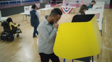 Erkek ABD vatandaşı seçim yapıyor ve oy kullanma kabininde oy kullanıyor. Amerika Birleşik Devletleri Başkanlık Seçimleri sırasında Afrikalı Amerikalı bir adam. Vatandaşlık görevi ve vatanseverlik. Yüksek açı.