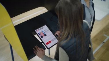 ZAPORIZHYA, UKRAINE - 15 Mart 2024: Kadın seçmen tablet bilgisayar kullanarak oy verme kabininde Joe Biden 'a oy veriyor. Başkanlık seçimlerinde oy kullanma merkezinde Amerikan vatandaşı