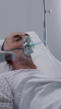 Hastane koğuşunda oksijen maskeli dikey bir adam. Akciğer ventilasyonu sırasında zatürree olan eski bir hasta. Klinikteki modern acil servis. Tıbbi tesiste yoğun bakım Coronavirus Bölümü
