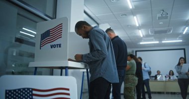 African American man votes in booth in modern polling station office. National Election Day in the United States. Political races of US presidential candidates. Concept of patriotism and civic duty. clipart