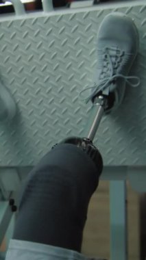 Modern spor salonunda protez bacaklı sporcunun bacak pres makinesinde dikey çekimi. Fiziksel engelli aktif atletik adam spor malzemelerini kullanarak egzersiz yapıyor. Vücut pozitif