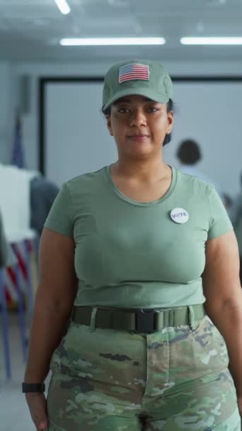 身着迷彩服的妇女站在投票站的垂直镜头 看着镜头 女兵的画像 美利坚合众国选举选民 设有投票箱的背景 — 图库视频影像