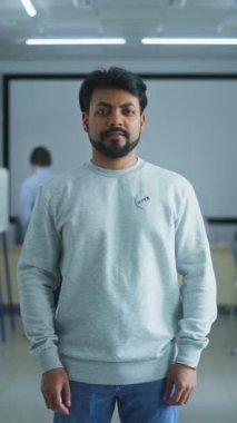 Amerika Birleşik Devletleri seçmeni Hintli adamın dikey çekimi. Adam modern bir seçim merkezinde duruyor, poz veriyor ve kameraya bakıyor. Oy verme kabinleri olan bir arka plan. Vatandaşlık görevi ve vatanseverlik