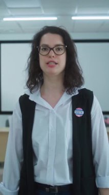 Amerikalı kadın seçmenin dikey çekimi ya da rozetli bir anket çalışanı kameraya konuşuyor, oylama çağrısı yapıyor. Birleşik Devletler 'de Ulusal Seçim Günü. Sandık merkezinde oy kullanma kabinleri. Civic