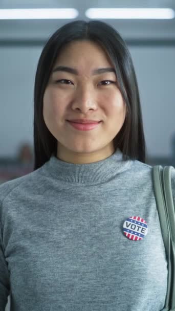 带着徽章的妇女站在现代投票站的垂直照片 摆出姿势 看着镜头 亚洲妇女的画像 美利坚合众国选举投票人 设有投票箱的背景 — 图库视频影像