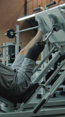 Modern fitness merkezinde protez bacaklı atletlerin bacak pres makinesinde dikey çekimi. Yapay bacaklı yetişkin sporcu profesyonel spor salonunu kullanarak güç egzersizleri yapıyor.