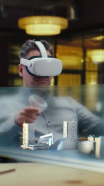 Erkek mimar sanal gerçeklikte metropolün mimari projesini yaratmak için VR kulaklık ve kablosuz kontrolör kullanıyor. Adam yüksek teknoloji şirketinde çalışıyor. Üç boyutlu hologram. Dikey çekim